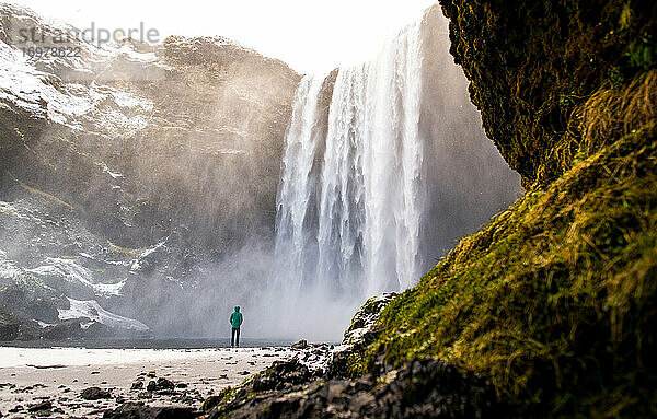 Person am Skogafoss-Wasserfall im Winter mit Moos im Vordergrund