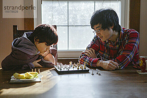 Ein Vater und sein Sohn studieren gemeinsam ein Schachbrett im Fensterlicht