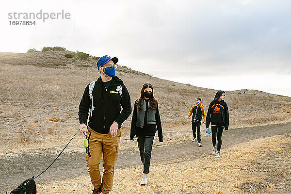 Vater und seine drei Kinder gehen auf eine Wanderung und tragen dabei Gesichtsmasken