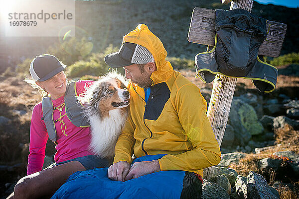 Mann und Frau Trailrunner füttern australischen Schäferhund und lächelnd