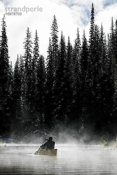Rückansicht eines Mannes beim Kanufahren auf einem See gegen Nebel und Bäume