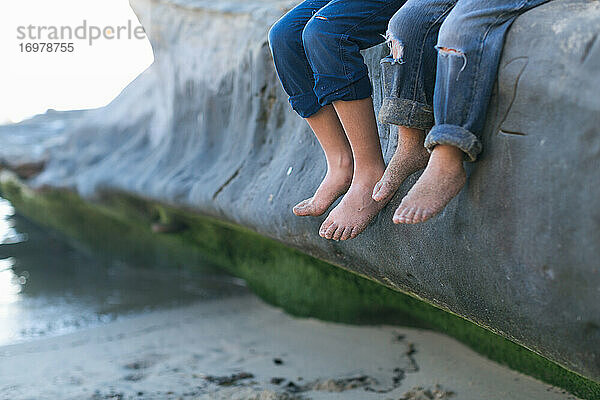 Brüder sitzen auf einem großen Felsen am Strand - Fokus auf ihre nackten Füße
