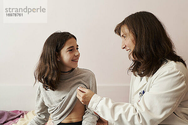 Weiblicher Arzt  der einem Mädchen in ihrem Bett die Temperatur auf einem Thermometer zeigt. Hausarzt Konzept