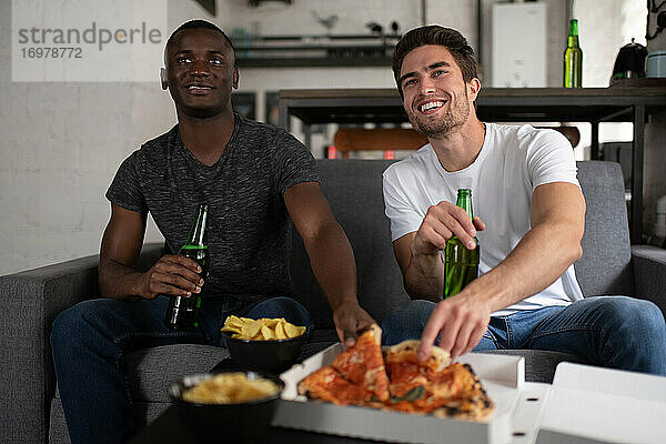 Fröhliche multiethnische Freunde essen Pizza und sehen sich ein Fußballspiel an