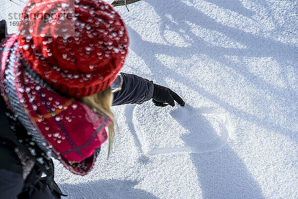 horizontale Draufsicht auf die Hand einer Frau  die einen roten Lederhandschuh trägt und mit dem Zeigefinger eine Herzform in den Schnee zeichnet  Konzept für Liebe  Winterzeit