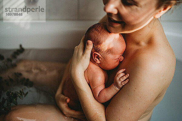 Glücklich lächelnde Mutter  die ihr neugeborenes Baby nach der Geburt zu Hause im Arm hält