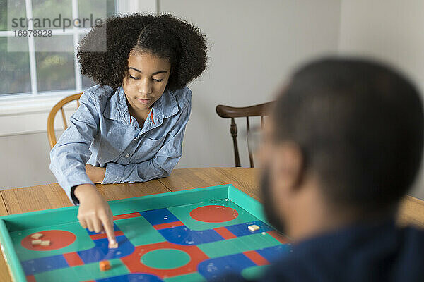 Ein zehnjähriges afroamerikanisches Mädchen spielt mit seinem Vater ein Brettspiel