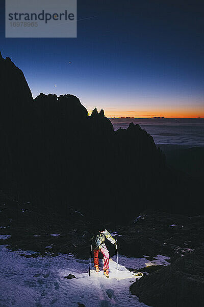 Junger Mann wandert vor Sonnenaufgang gegen Berge und Mondsichel zum Gipfel  Gredos  Spanien