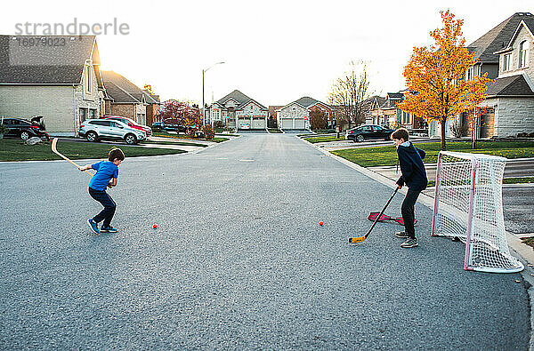 Zwei Jungen spielen Streethockey in einer Wohnstraße im Herbst.