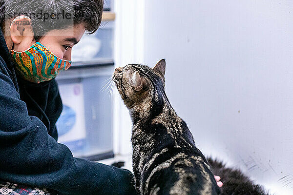 Katze trifft ein Kind  das eine Maske trägt  für Pandemie-Adoptionen im Tierheim