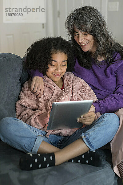 Kaukasische Mutter und gemischtrassige Tochter im Vorschulalter schauen gemeinsam auf das iPad