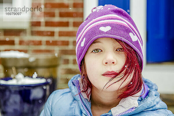 Hübsches kleines Mädchen mit leuchtend rot gefärbtem Haar sitzt draußen im Winter