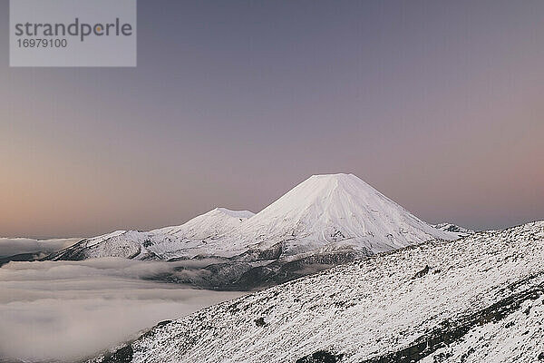 Der Berg Ngauruhoe über dem Nebel im Tongariro-Nationalpark im Winter in pastellfarbenen Lila-Tönen gefärbt