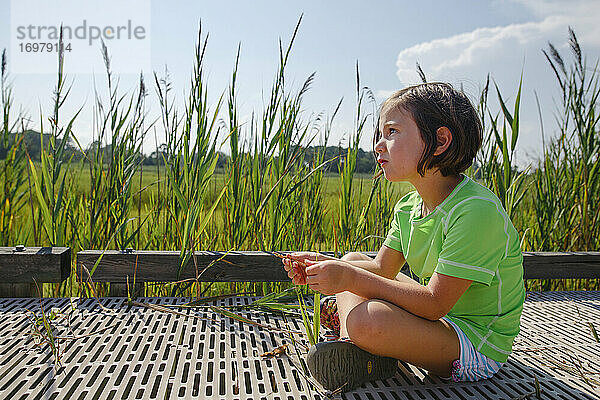 Ein süßes kleines Mädchen sitzt auf der Promenade in einem Feuchtgebiet mit hohem Gras