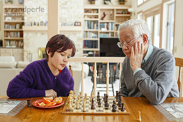 Ein Junge mit gefärbten roten Haaren sitzt mit seinem Großvater am Tisch und spielt Schach