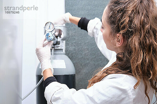 Junge Wissenschaftlerin beim Öffnen einer Gasflasche mit Manometer in einem Speziallabor. Konzept der Laborforschung.