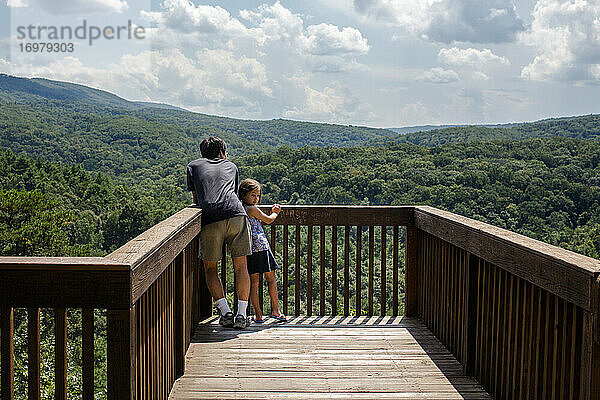 Ein kleines Kind lehnt sich an den Vater auf der Plattform mit Blick auf den Wald