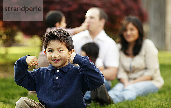 Junge  der vor seiner Familie im Gras sitzt und sich beugt