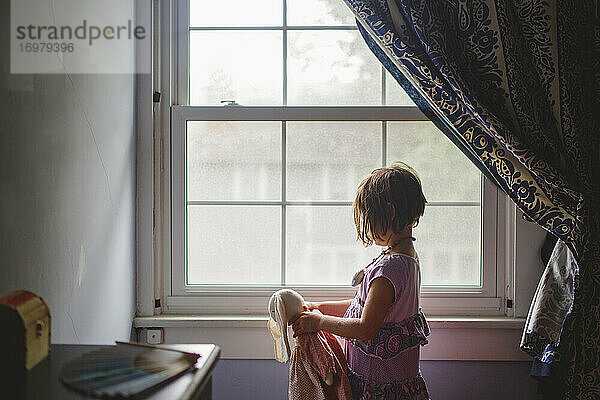 Ein kleines Kind steht im Fensterlicht und hält ein Stofftierhäschen