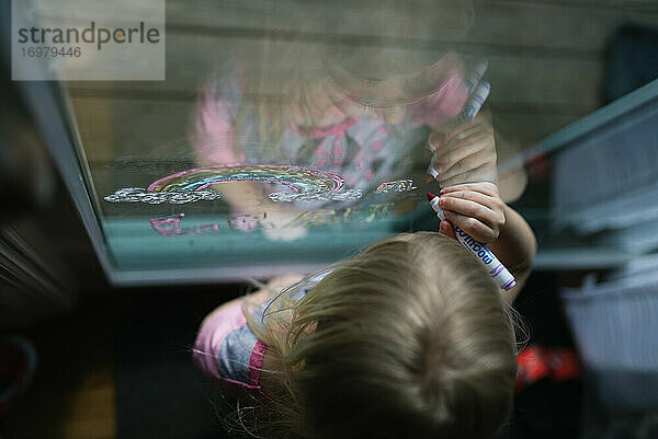 Draufsicht auf ein Kind  das mit Filzstiften am Fenster malt