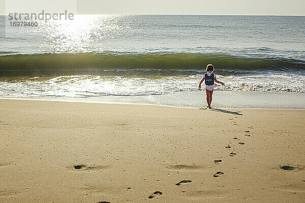 Ein kleines Mädchen läuft über goldenen Sand am Strand zum Meer