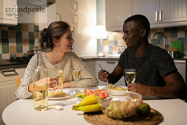 Multiethnisches Paar  das abends zu Hause Nudeln isst