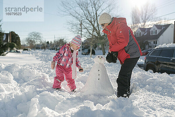 Großmutter und Enkelin bauen Schneemann im Vorgarten