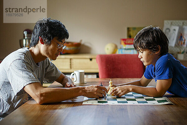 Ein Vater und sein Sohn sitzen an einem Tisch und spielen eine Partie Schach.