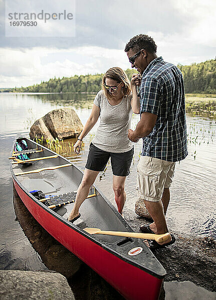 Ein Afroamerikaner hilft einer weißen Frau in ein rotes Kanu auf einem See.