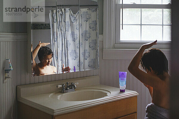 Ein in ein Badetuch eingewickelter Junge schaut in den Spiegel und trägt Haargel auf