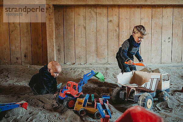Kinder spielen mit Lastwagen und Baggern im Wintersandkasten im Freien