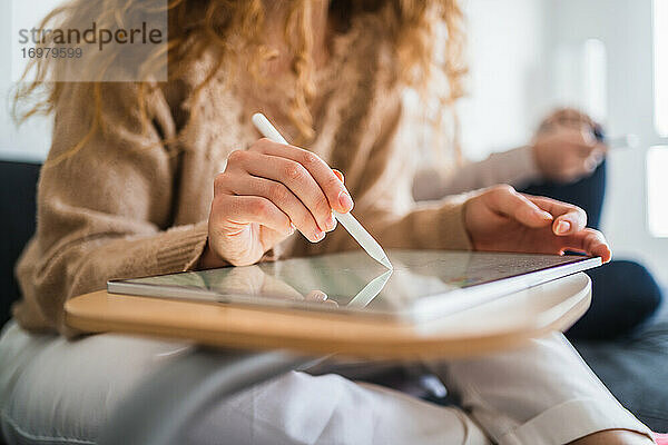 Junge anonyme Designerin  die in der Nähe ihres Freundes auf einem Tablet zeichnet