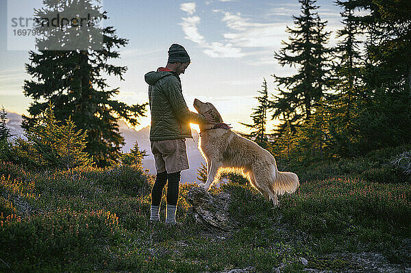 Männlicher Wanderer streichelt Hund bei Sonnenuntergang in den Bergen