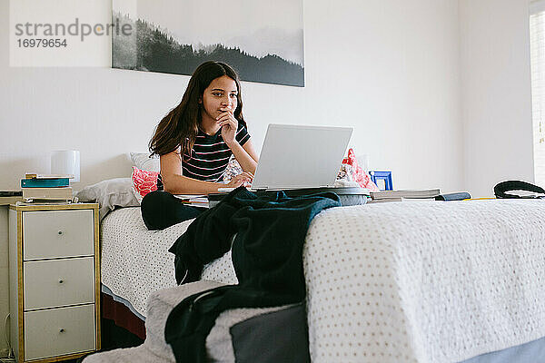 Tween Girl arbeitet auf ihrem Laptop während der Online-Schule auf ihrem Bett