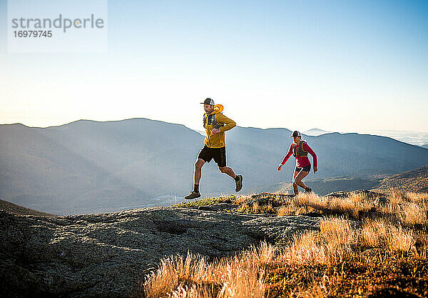 Mann und Frau beim Trailrunning in den Bergen bei Sonnenaufgang