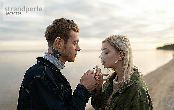 Junger Mann und Frau rauchen am See