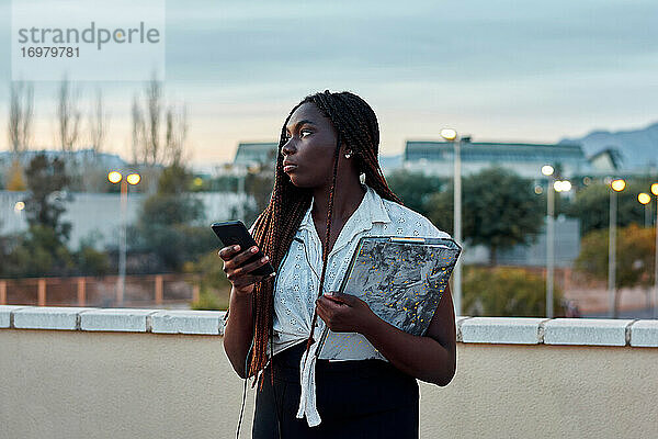 Junge afrikanische Studentin benutzt ihr Handy und hält einen Ordner