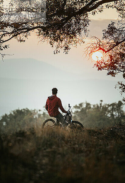 Junger Biker auf seinem Fahrrad sitzend bei Sonnenuntergang im Herbst
