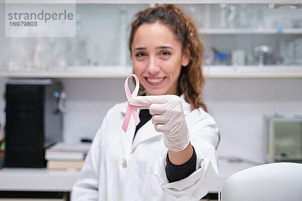 Junge Wissenschaftlerin  die eine rosa Schleife vor ihrem Gesicht hält  um auf Brustkrebs aufmerksam zu machen. Krebsforschung Konzept.