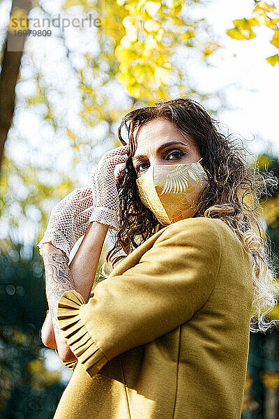 Frau in gelbem Kleid und Maske in einem Park im Herbst