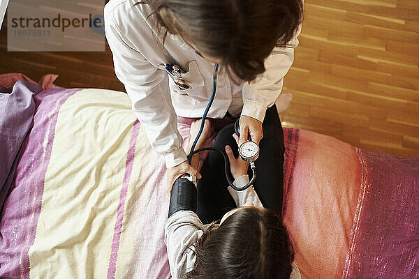 Draufsicht auf eine Ärztin  die den Druck auf den Arm eines Mädchens in ihrem Bett untersucht. Hausarzt Konzept