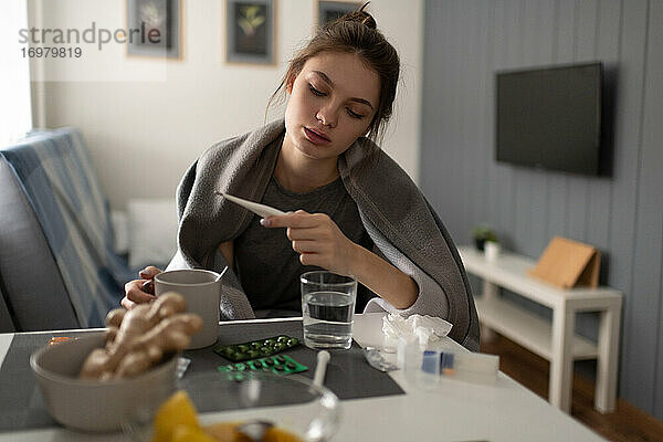 Kranke Frau mit Tee zur Kontrolle des Thermometers