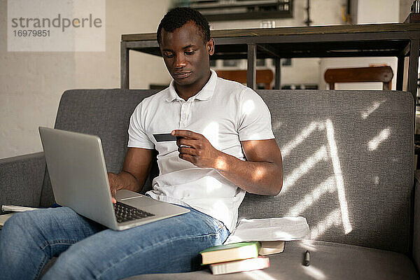 Afroamerikanischer Student  der auf dem Sofa sitzend online einkauft
