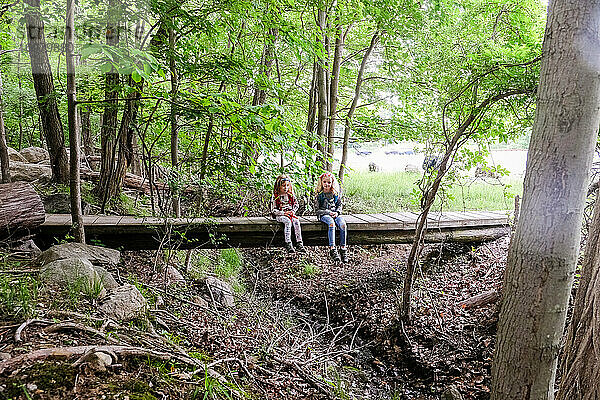 zwei Mädchen sitzen zusammen und ruhen sich beim Wandern auf einer Brücke im Wald aus