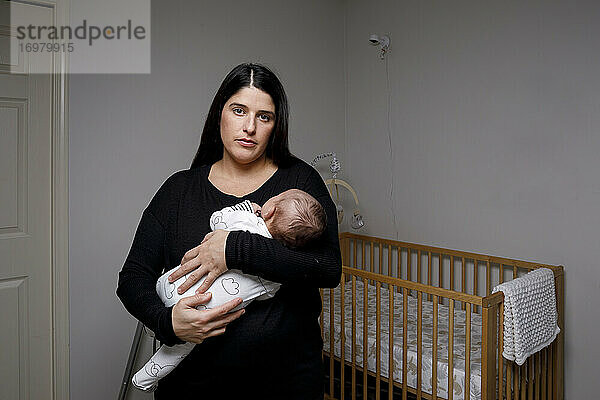 Eine Mutter hält ihren neugeborenen Sohn in den Armen im Kinderzimmer und schaut in die Kamera