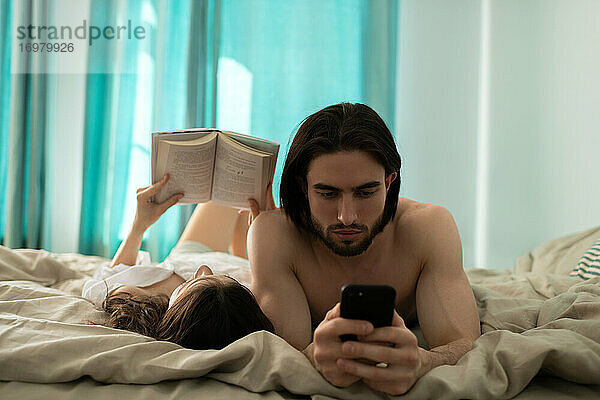 Junger Mann schaut auf sein Smartphone  während seine Freundin Boo liest