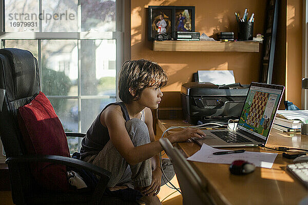 Ein Junge im Teenageralter sitzt am Computer und spielt ein Online-Schachspiel am Schreibtisch