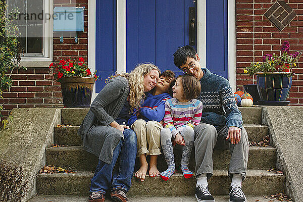 Eine liebevolle Familie kuschelt sich im Herbst auf der Treppe vor dem Haus zusammen