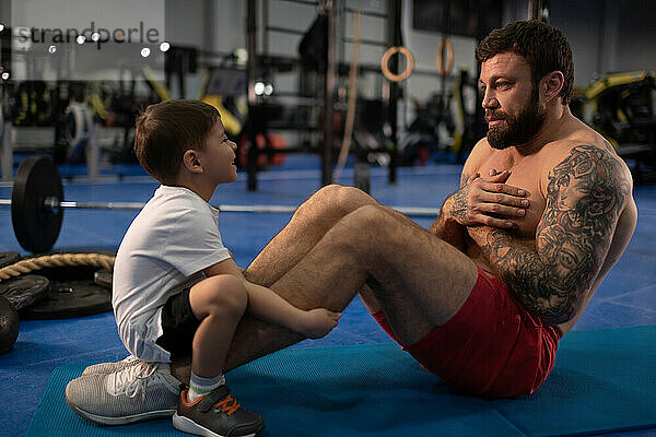 Glücklicher Sohn hilft Vater bei Bauchmuskelübungen