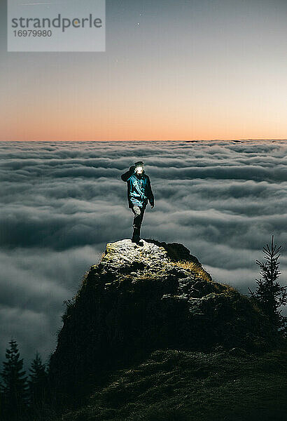 Person stehend auf dem Berg über den Wolken mit Taschenlampe
